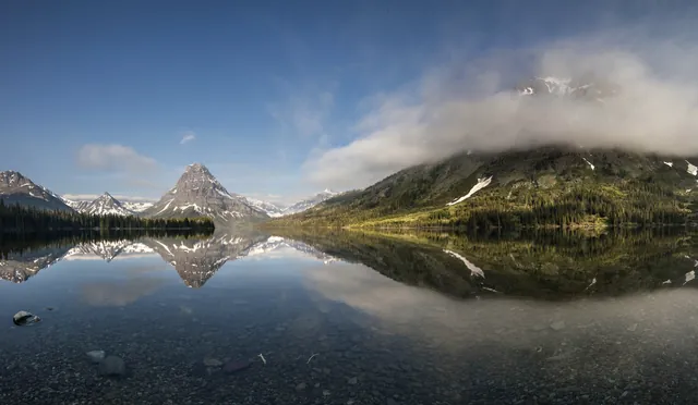 Snow-speckled mountains reflected into a calm lake.