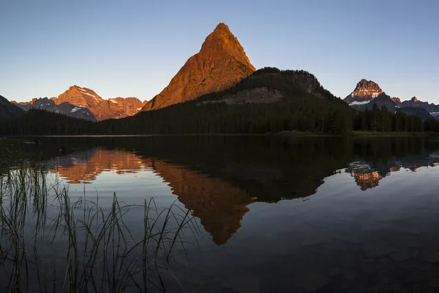 Golden morning light hit a mountain, which is reflected onto a smooth lake.